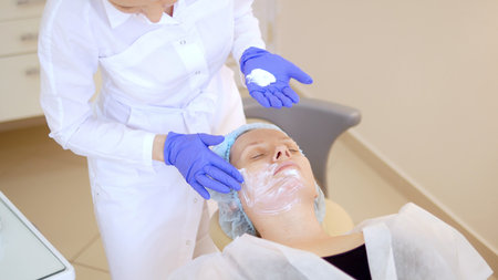 concept beautician. The hands of a cosmetologist put cream on the face of a woman. Beautician applies a cream to the face of the girlの写真素材