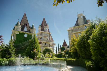 modern Victorian-style luxury hotel with a small fountain at the foot, beautiful well-kept trees against a blue sky in clear sunny weatherの写真素材