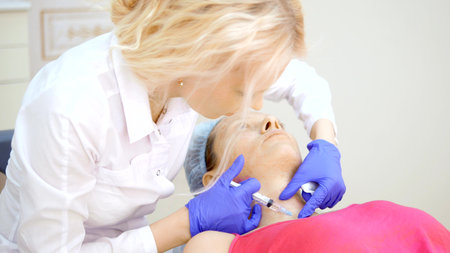 The cosmetologist makes injections, anti-aging procedures for tightening and smoothing wrinkles on the skin of the face and neck of a woman.の写真素材