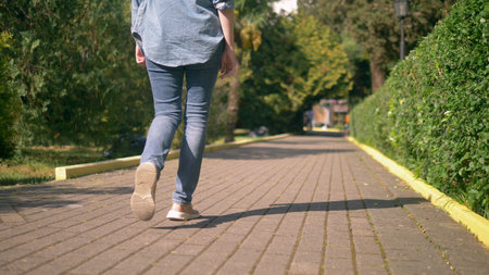 womens legs in jeans and sneakers are on a paved pathの写真素材