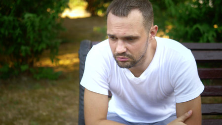 Depressed Sad young man sitting alone on a bench in a summer park. copy spaceの写真素材