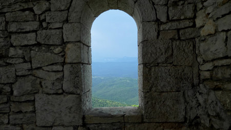 stone wall and arched window openings with a view of a mountain range with forest and haze over the...
