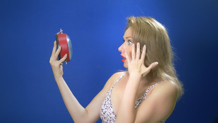 Surprised pin-up woman holding clock. Amazed pinup girl. Saving time concept. Summer sale. Discount. blue background Copy space. Expressive facial expressions.の写真素材