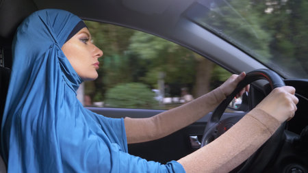 beautiful muslim woman in blue hijab driving a car. rides during the day on the streets of the city.