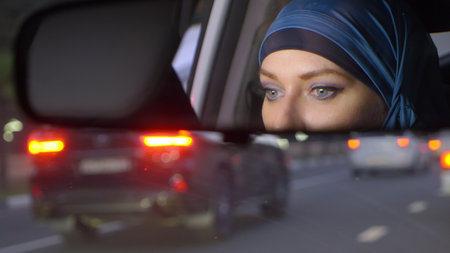 reflection of a woman in a hijab in a rearview mirror of a car while driving in a traffic jam in the evening. Muslim woman driving a car.の写真素材