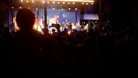 rock concert in the evening. people in the crowd raise their hands and applaud. blurred background, silhouettes of fans.の写真素材