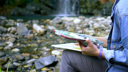 close-up. Woman artist . hands on nature against the backdrop of a waterfall. paint in the palette.の写真素材