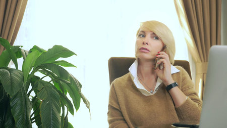 Woman in office talking on the phone looking at laptopの写真素材