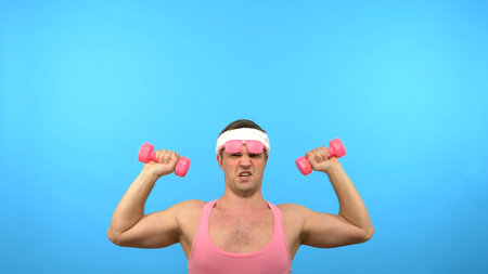 Playful handsome man in a pink shirt is engaged in fitness with pink dumbbells. Bright Fitness. Sports fashion accessoriesの写真素材