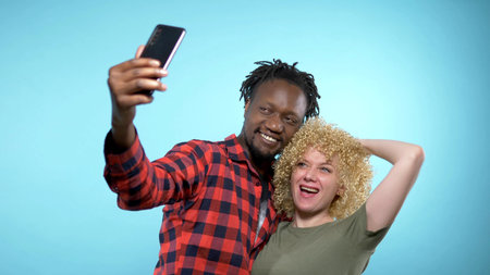 African guy and caucasian girl making selfie with smartphone. blue background.