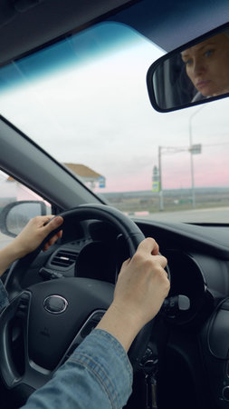 vertical shot of female hands on the steering wheel of a moving car