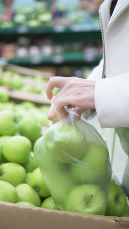 vertical shot. closeup of hands. woman picks green apples in the supermarketの写真素材