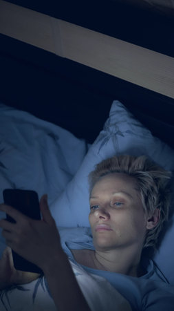 vertically. woman suffering from insomnia uses a smartphone while lying in bedの写真素材