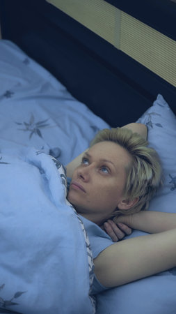 vertical. a woman suffering from insomnia lies in bed in the darkの写真素材