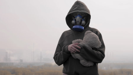 girl in respirator with a soft toy on the background of Smoking factory chimneysの写真素材