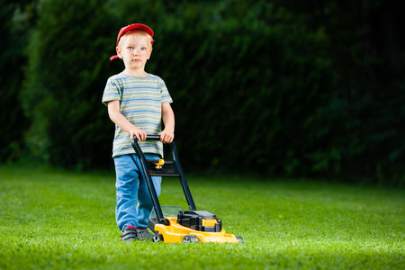 Cute boy mows lawn by yellow lawn mowerの写真素材