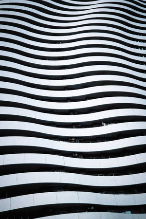 A professional architectural shot focusing on the repetitive, wave-like structure of a skyscraper's balconies. The high-contrast composition highlights the flowing white lines of the terraces against the dark shadows of the windows, creating a mesmerizing rhythmic pattern.の写真素材