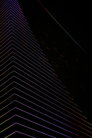 A professional night photograph of two modern skyscrapers defined by glowing horizontal LED light...