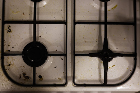 A professional top-down shot of a white gas stovetop covered in grease splatters, dried food particles, and stains. The image captures the state of a kitchen before cleaning, emphasizing the importance of home maintenance and sanitary standards.の写真素材