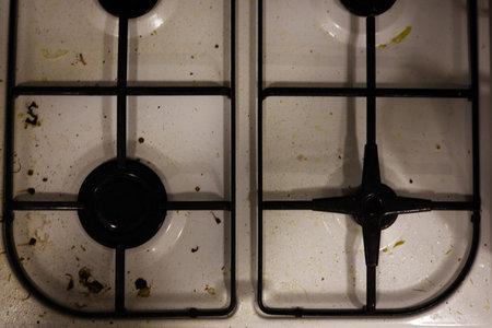 A professional top-down shot of a white gas stovetop covered in grease splatters, dried food particles, and stains. The image captures the state of a kitchen before cleaning, emphasizing the importance of home maintenance and sanitary standards.の写真素材