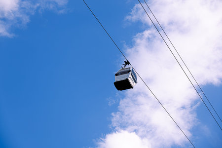Single cable car cabin moving along an aerial ropeway against a cloudy sky. Modern public transportation system used for tourism and urban mobility, captured in a minimalist composition emphasizing engineering, travel and infrastructure.