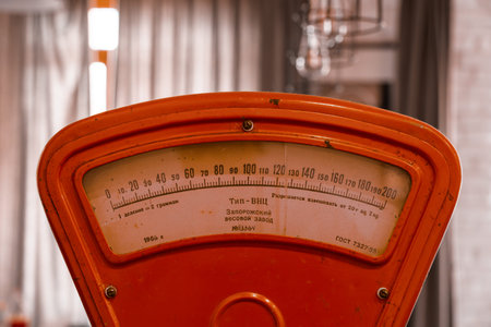 Detailed close up of a vintage red mechanical weighing scale with worn metal surfaces and classic analog display. Antique retail equipment symbolizing traditional commerce, measurement, nostalgia, craftsmanship and retro interior decor.