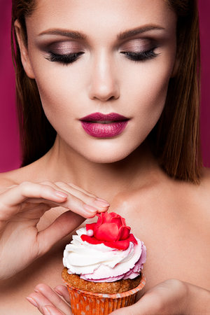 Beautiful fashion girl with bright make up, handing cupcake.の写真素材