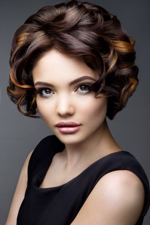 Glamour portrait of beautiful girl model with makeup and romantic wavy hairstyle. Fashion shiny highlighter on skin, sexy gloss lips make-up and dark eyebrows.の写真素材