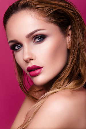 Beautiful young woman with long hair posing on pink shiny background. Healthy skin and long smooth hair. Pink lipsの写真素材