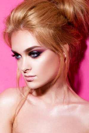 Close-up portrait of beautiful woman with bright make-up and hairstyle. Pink background.の写真素材