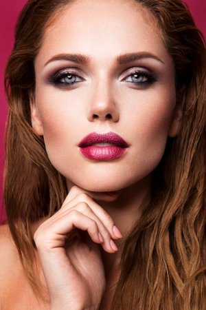 Glamour portrait of beautiful girl model with makeup and romantic wavy hairstyle. Fashion shiny highlighter on skin, sexy gloss lips make-up and dark eyebrows.の写真素材