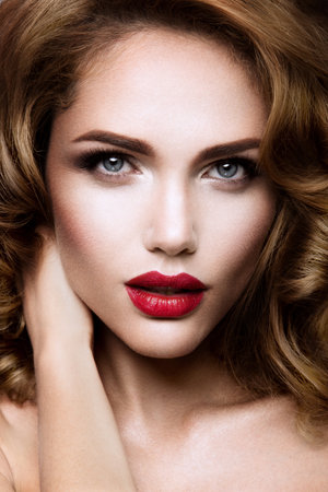 Glamour portrait of beautiful girl model with makeup and romantic wavy hairstyle. Fashion shiny highlighter on skin, sexy gloss lips make-up and dark eyebrows.の写真素材