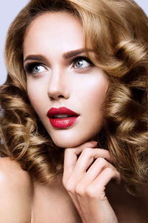 Glamour portrait of beautiful girl model with makeup and romantic wavy hairstyle. Fashion shiny highlighter on skin, sexy gloss lips make-up and dark eyebrows.の写真素材