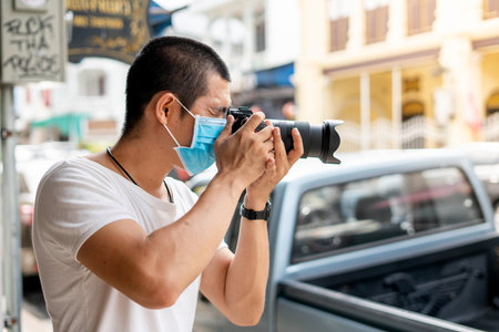 Asian man is wearing surgical mask while holding a camera during covid19 or corona virus spreadの写真素材