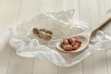 The crude peanuts on a wooden spoon. Nuts are located on a white crumpled paper texture on a wooden...