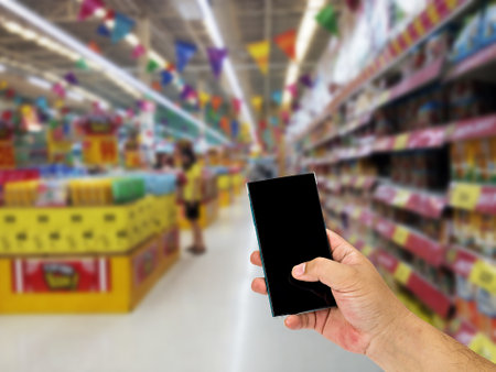 Man hand holding smart phone over blurred shopping center or super market background.