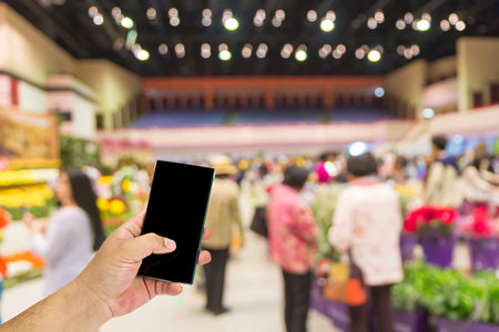 Man hand holding smart phone over blurred shopping center or super market background.の写真素材