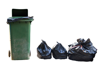 Old large green wheel bin and pile of full garbage bagsの写真素材