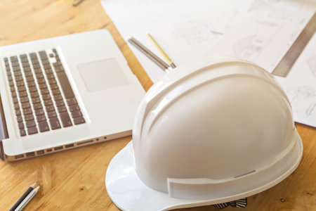 Close up of helmet  with architect sketching a construction project and laptop