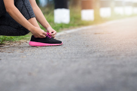 sport, fitness, people and lifestyle concept - close up of woman tying shoelaces outdoors