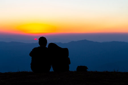 Sweet couple silhouette sitting on the mountain with sunset backgroundの写真素材