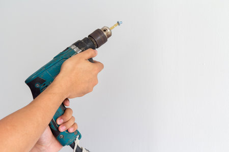 Man hands hold electric drill on white wall