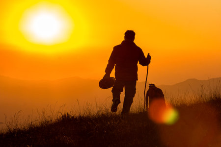 Silhouettes of traveller walking on mountain with sun flareの写真素材