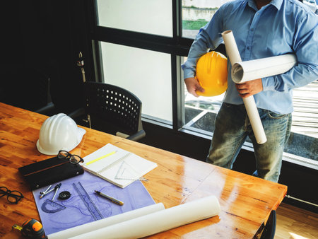 Architect with blueprint and helmet on wooden desk