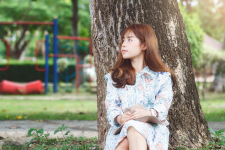 Pretty asian girl sitting leaning against on the tree relaxing.の写真素材