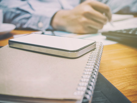 Close up of smartphone on notebook with businessman backgroundの写真素材