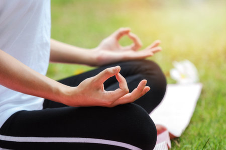 Young asian woman in sportswear meditating while sitting in lotus pose on yoga matの写真素材