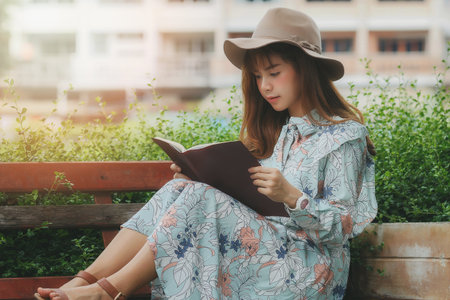 Young asian woman reading a book on the bench in parkの写真素材
