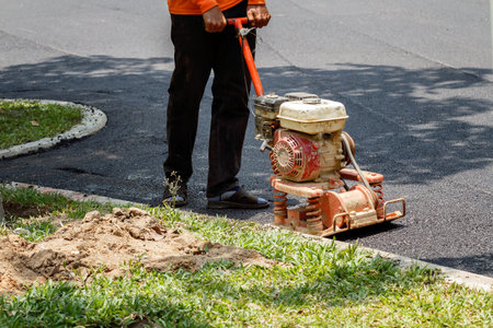 Worker uses vibratory plate compactor compacting asphalt at road repair