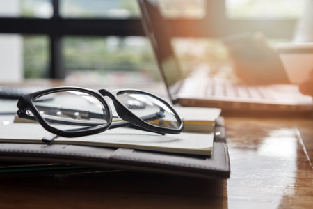 eyeglasses on notebook near window backgroundの写真素材